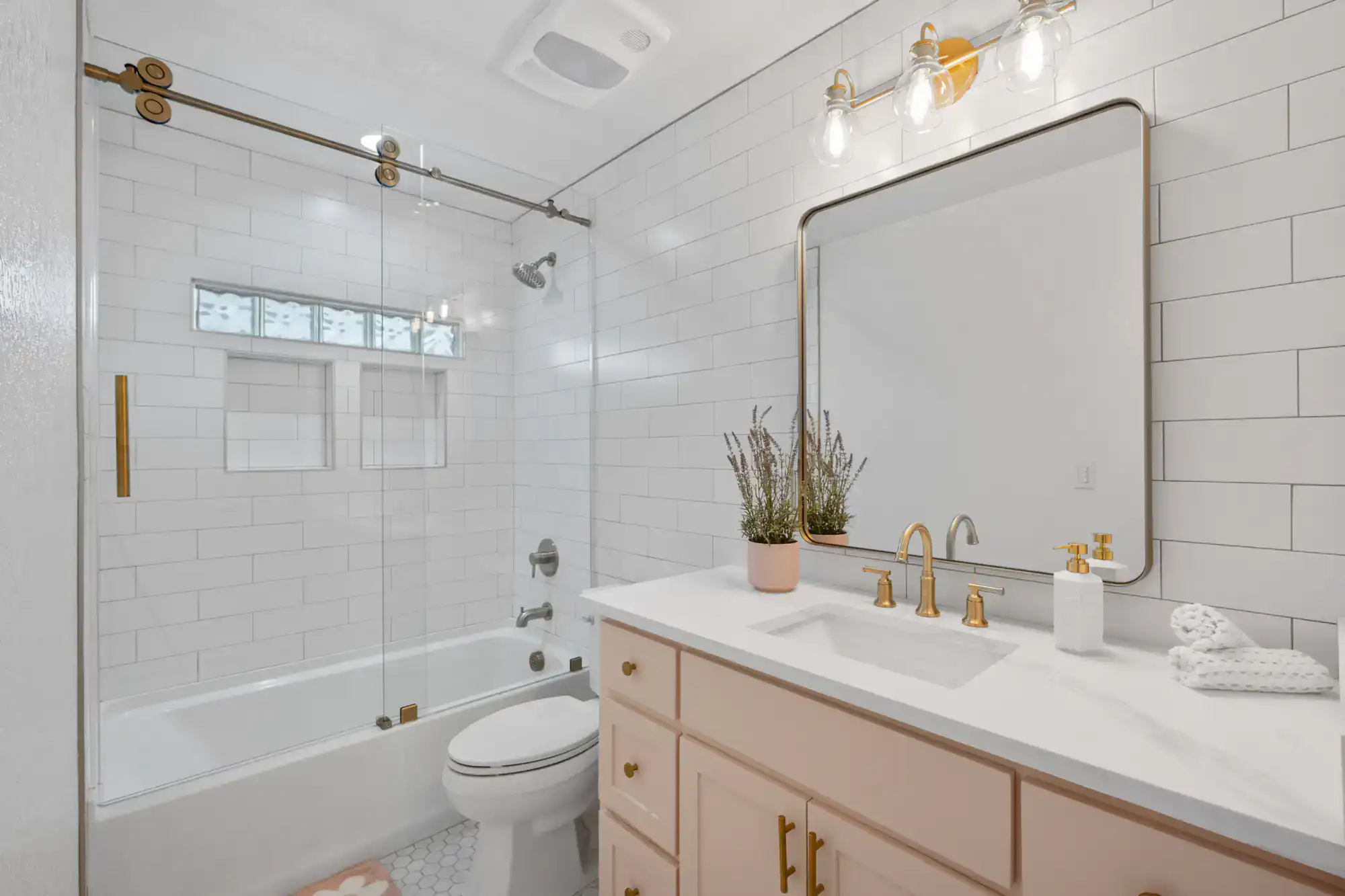 Contemporary bathroom with white tiles, gold fixtures, and a large mirror.