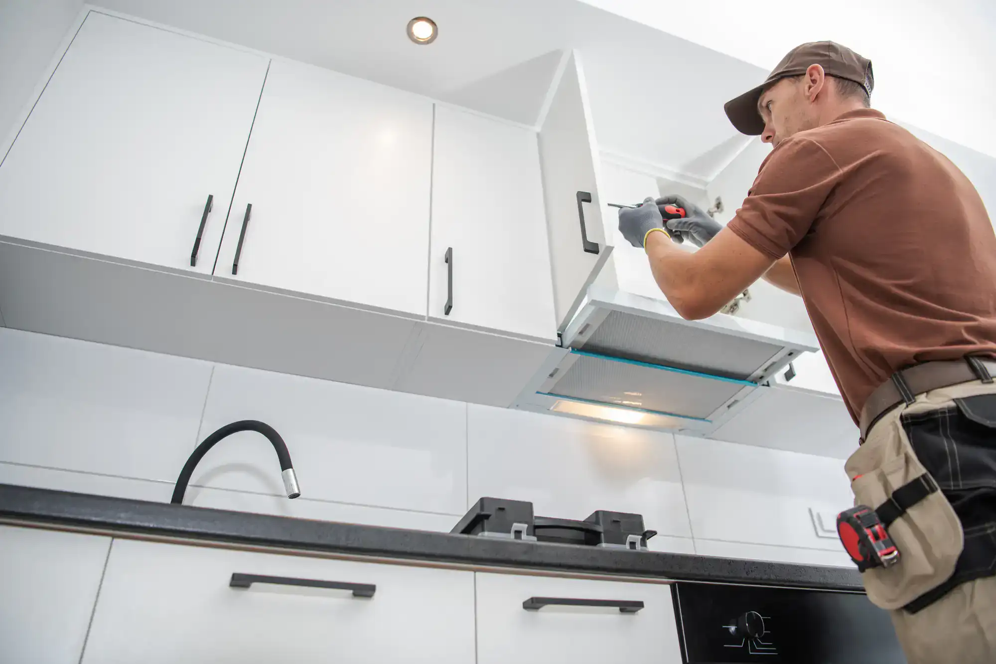 Professional installer fixing kitchen range hood in a modern kitchen.