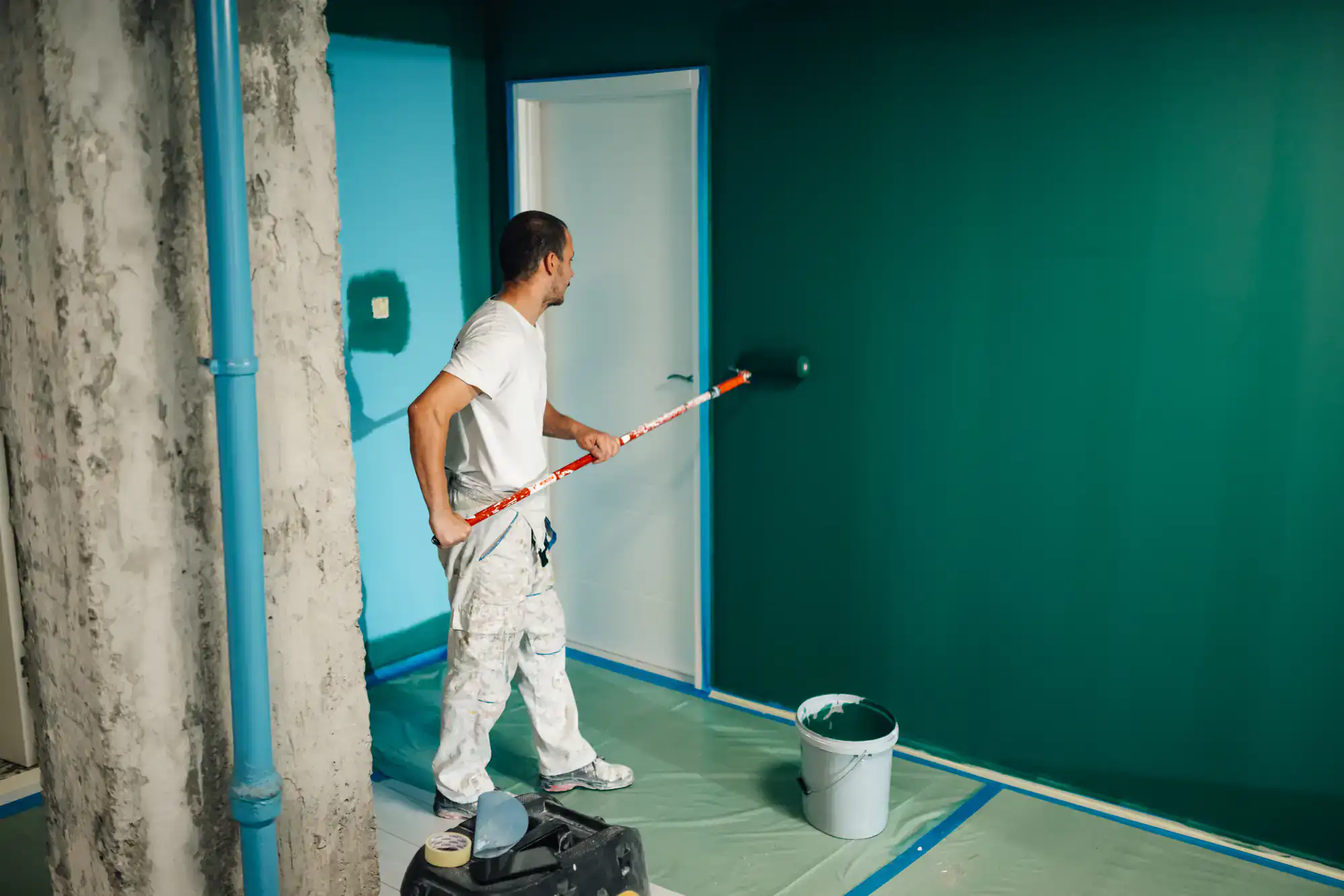 Painter applying green paint to wall in a room under renovation.