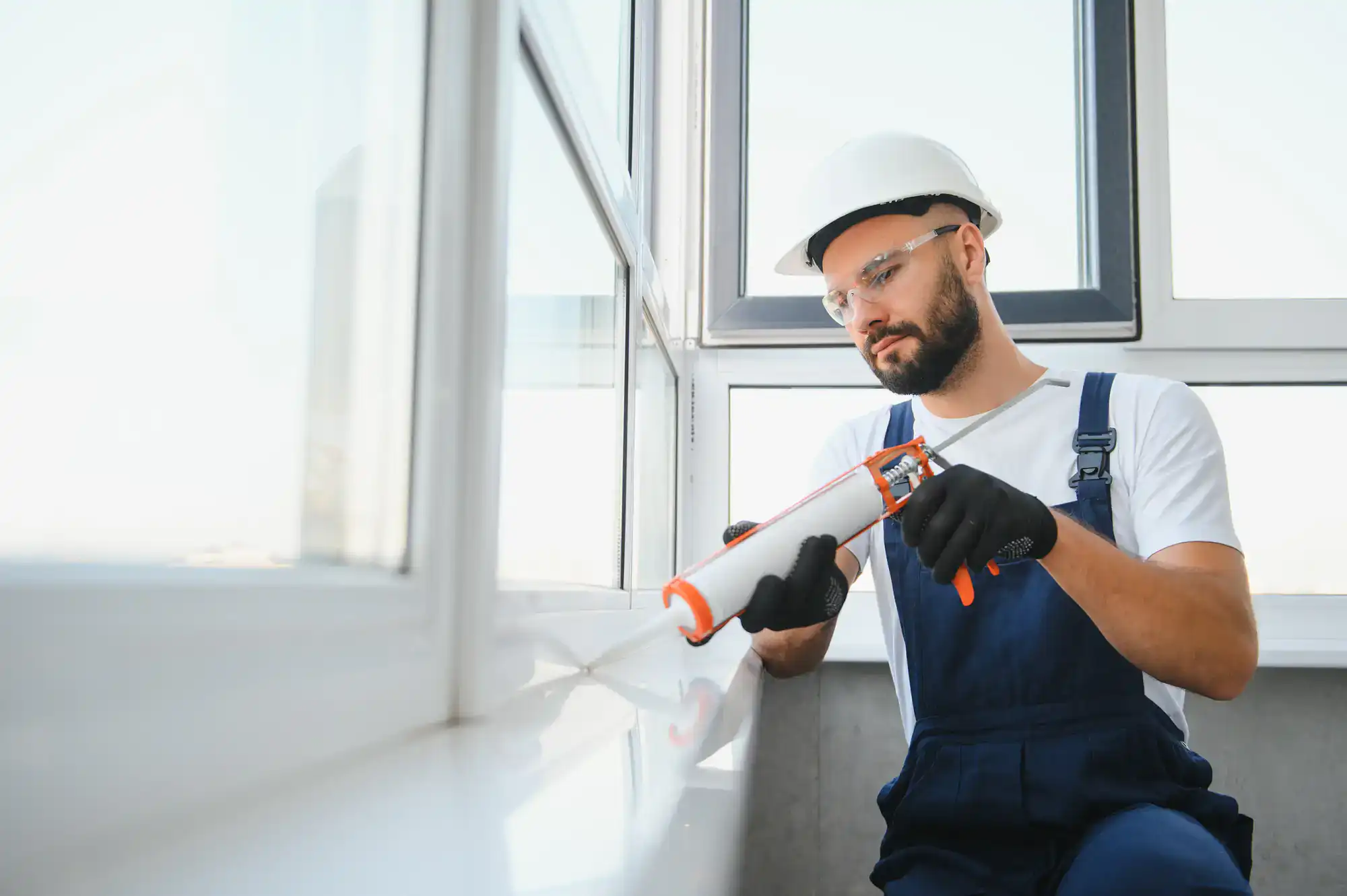 Professional worker sealing window with caulk for insulation.