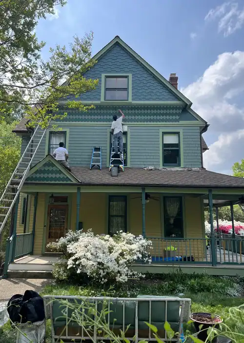 Exterior house painting in progress with workers on ladder and scaffolding.